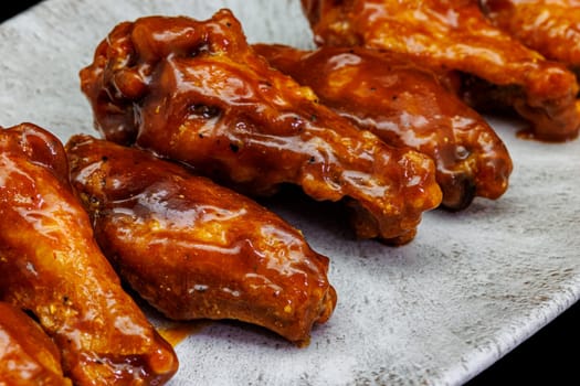 Composition of a plate of chicken wings with barbecue sauce on black background