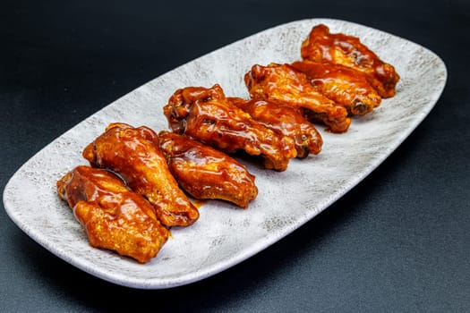 Composition of a plate of chicken wings with barbecue sauce on black background