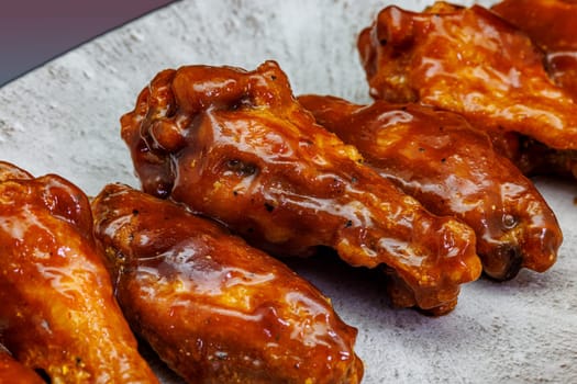 Composition of a plate of chicken wings with barbecue sauce on a magenta and light blue gradient background