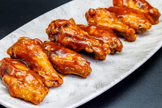 Composition of a plate of chicken wings with barbecue sauce on black background