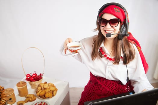 Portrait of young girl in a bright red scarf and large headphones with a microphone. A woman who is radio or television presenter with cap of tee. Funny female telecom operator. Freelancer at work