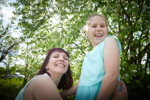 Happy mother and daughter enjoying rest, playing and fun on nature on a green lawn and with blooming apple tree in the background. Woman and girl resting outdoors in summer and spring day