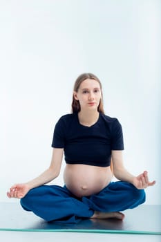 Pleasant pregnant woman posing in profile and trying yoga Young happy expectant relaxing, thinking about her baby and enjoying her future life. Motherhood, pregnancy, yoga concept, lotus position.