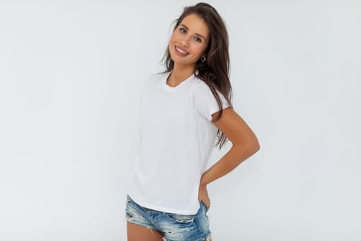 Beautiful brunette girl in a white T-shirt and denim shorts posing on a white background. High quality photo