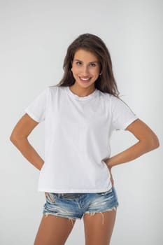 Beautiful brunette girl in a white T-shirt and denim shorts posing on a white background. High quality photo