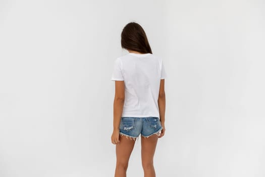 Beautiful brunette girl in a white T-shirt and denim shorts posing on a white background. High quality photo