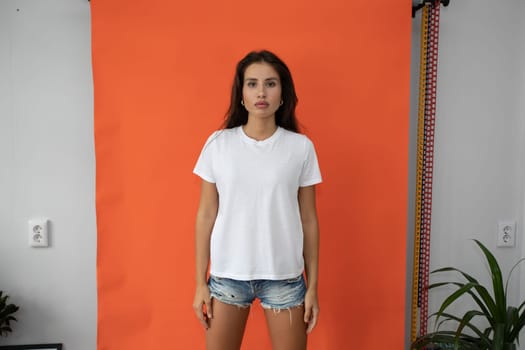 Beautiful brunette girl in a white T-shirt on an orange background. High quality photo