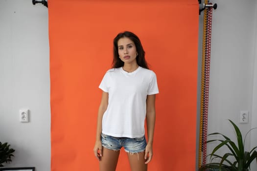 Beautiful brunette girl in a white T-shirt on an orange background. High quality photo