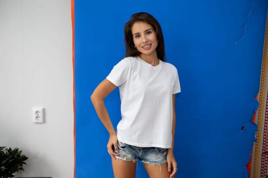 Beautiful brunette in a white T-shirt and shorts posing on a blue background. High quality photo