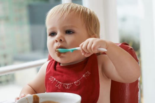 Hungry, sweet and baby eating porridge for health, nutrition or child development at home. Food, cute and girl toddler or kid enjoying an organic puree meal for lunch or dinner in high chair at house.