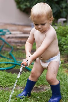 Baby, playing with hose and water, backyard and development with growth, curiosity and home. Toddler, child and infant in garden, alone and childhood for wellness, milestone and coordination.