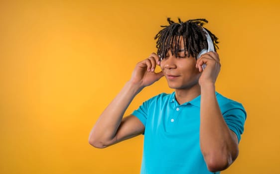 Positive young african american man listening music, enjoying dance with headphones on yellow studio background. Radio, wireless modern sound technology, online player. High quality.