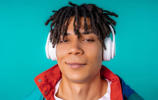 Positive young african american man listening music, enjoying dance with headphones on blue studio background. Radio, wireless modern sound technology, online player. High quality.