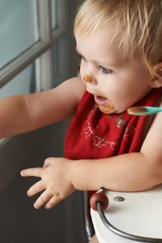 Cute, feeding and baby eating porridge in high chair for nutrition, health and wellness at home. Sweet, playing and girl kid, infant or toddler enjoying puree food for child development at house