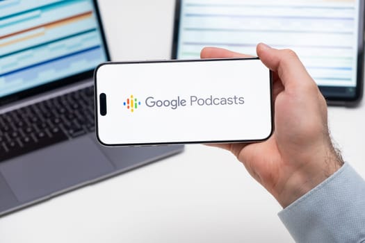 Google Podcast logo of app on the screen of mobile phone held by man in front of the laptop and tablet, December 2023, Prague, Czech Republic