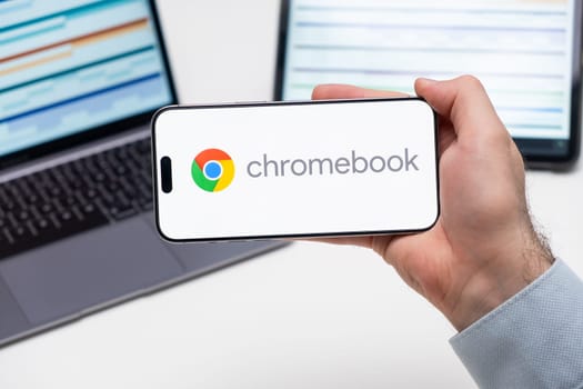 Chromebook logo of app on the screen of mobile phone held by man in front of the laptop and tablet, December 2023, Prague, Czech Republic