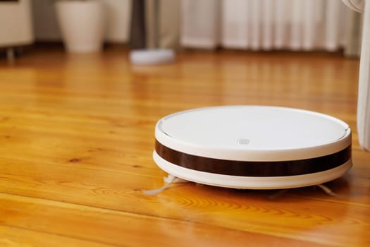 Smart home cleaning technology concept with a robotic vacuum cleaner operating on a shiny wooden floor.