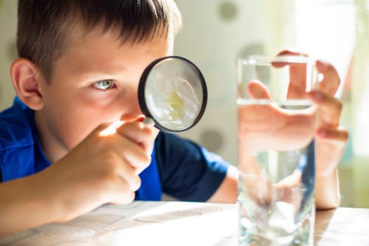 Curious child examines water in a glass with a magnifying glass, focusing on science and discovery
