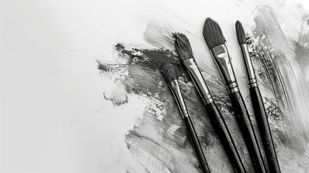 artistic array of paintbrushes with black bristles, lying over a canvas with expressive grey and black brush strokes, conveying a monochromatic artistic process, banner with copy space