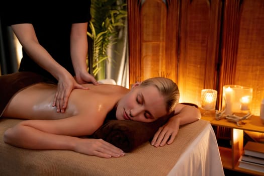 Caucasian woman customer enjoying relaxing anti-stress spa massage and pampering with beauty skin recreation leisure in warm candle lighting ambient salon spa at luxury resort or hotel. Quiescent