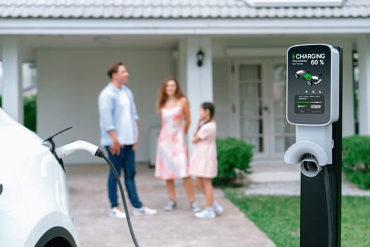 Focused electric vehicle recharging battery from home charging station for EV car powered by alternative and sustainable energy for modern environmental family on blurred background. Synchronos