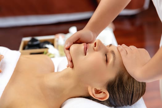 Caucasian woman enjoying relaxing anti-stress head massage and pampering facial beauty skin recreation leisure in dayspa modern light ambient at luxury resort or hotel spa salon. Quiescent