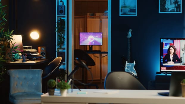 Computer screens showing abstract animation rendering in dimly lit empty home interior. 3D renders on digital displays in neon illuminated cozy apartment living room with TV running in background