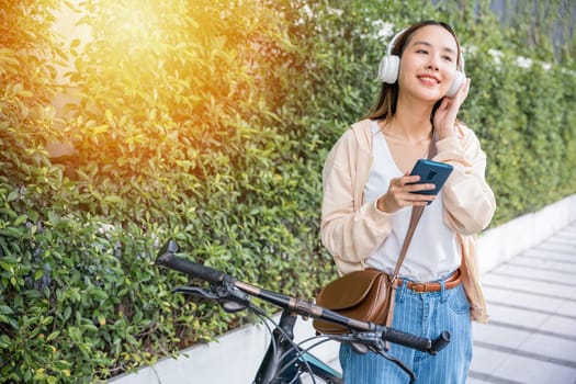 A cheerful woman with her bicycle takes leisurely walk in park on splendid spring day. She listens to music through earphones types joyful message on her mobile phone and epitomizes beauty of season.