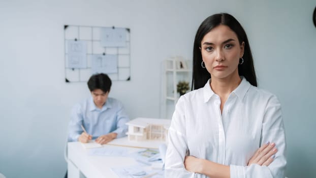 Closeup of female professional architect engineer cross arms with confident while skilled coworker focus on drawing blueprint at table with house model. Creative living and design concept. Immaculate.