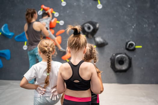 Rear view of three girls in activewear watching coach during wall climbing class. Sporty female children on climbing session. Young girls represent health and fitness concepts.