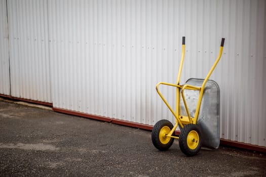 a yellow wheelbarrow stands by the wall. High quality photo