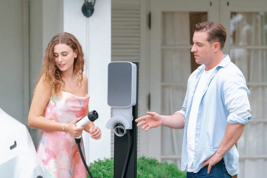 Happy and lovely couple with eco-friendly conscious recharging electric vehicle from EV home charging station. EV car technology utilized for residential home to future sustainability. Synchronos