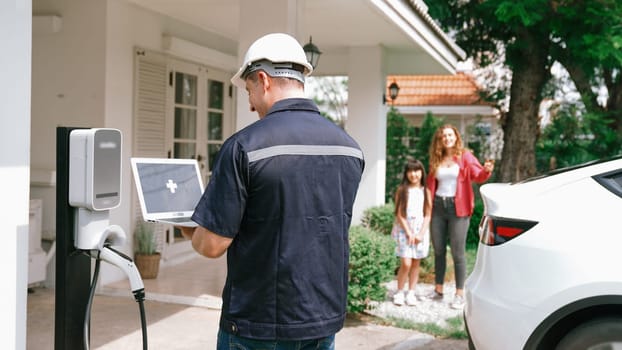 Qualified technician working on home EV charging station installation, making troubleshooting and configuration setup on charging system with empty laptop screem for EV at home. Synchronos