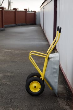 a yellow wheelbarrow stands by the wall. High quality photo