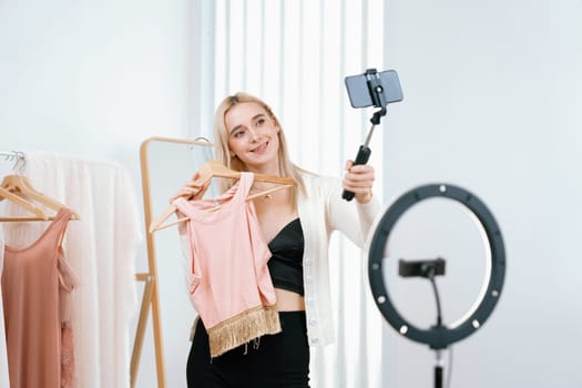 Young social medial content creator woman make fashion video. Blogger smiles to camera and light ring while making persuasive online clothing sell vlog to audience or follower. Blithe