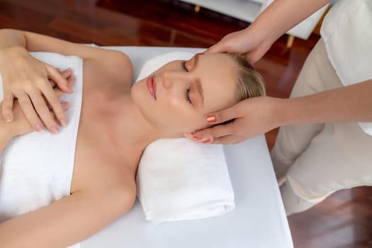 Caucasian woman enjoying relaxing anti-stress head massage and pampering facial beauty skin recreation leisure in dayspa modern light ambient at luxury resort or hotel spa salon. Quiescent