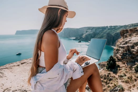 Digital nomad, Business woman working on laptop by the sea. Pretty lady typing on computer by the sea at sunset, makes a business transaction online from a distance. Freelance remote work on vacation