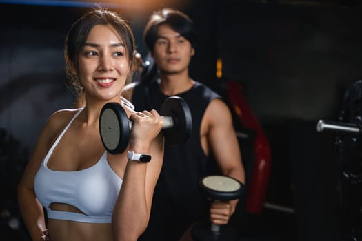 A fit couple in black workout clothes, smiling cheerfully while holding dumbbells, works together to build their muscular bodies and achieve their fitness goals. lifestyle fitness concept