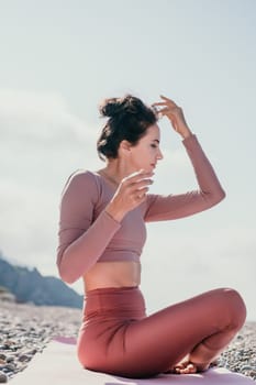 Young woman with long hair in white swimsuit and boho style braclets practicing outdoors on yoga mat by the sea on a sunset. Women's yoga fitness routine. Healthy lifestyle, harmony and meditation