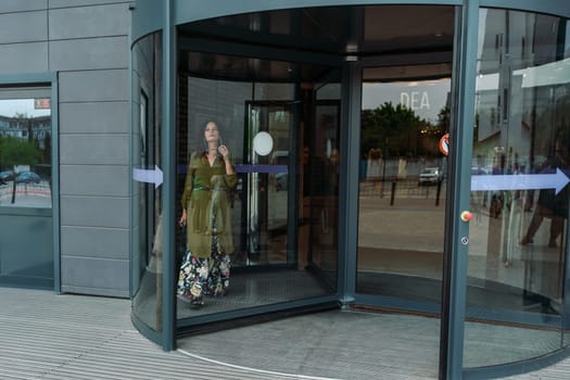 Woman leaves a supermarket. Caucasian model with long brunette hair, wears sunglasses and a khaki dress.