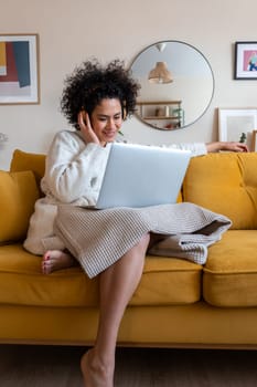 Happy African american woman watching movie with laptop and headphones sitting on the couch relaxing at home. Vertical image. Technology concept.