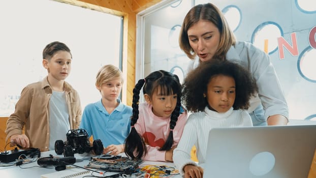 Caucasian teacher praise student while looking at learner work or presentation. Group of diverse student looking at presentation and fixing motherboard at table with chips and wires placed. Erudition.