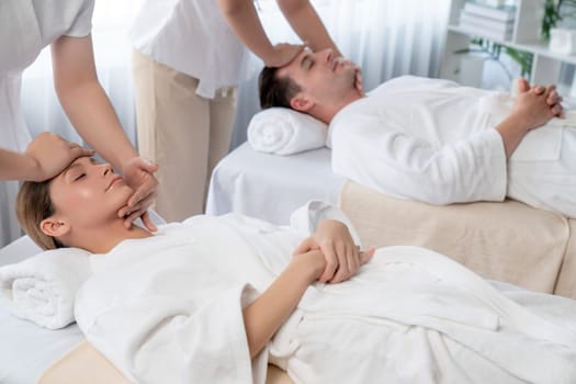 Caucasian couple enjoying relaxing anti-stress head massage and pampering facial beauty skin recreation leisure in dayspa modern light ambient at luxury resort or hotel spa salon. Quiescent