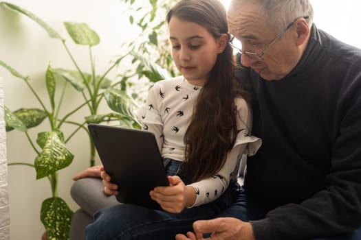 Senior man with his grandchild looking together on photos in tablet.