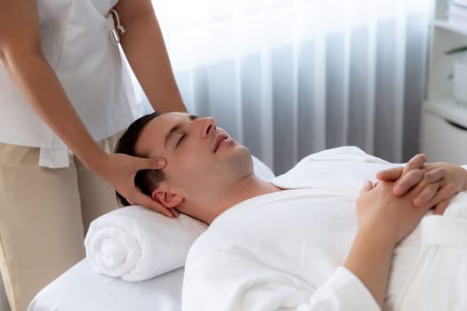 Caucasian man enjoying relaxing anti-stress head massage and pampering facial beauty skin recreation leisure in dayspa modern light ambient at luxury resort or hotel spa salon. Quiescent