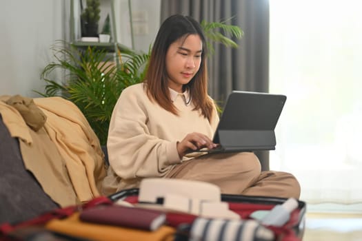 Young woman planning for trip with digital tablet, getting ready for holidays travel trip in living room.