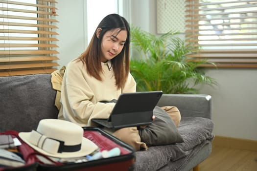 Young woman planning for trip with digital tablet, getting ready for holidays travel trip in living room.