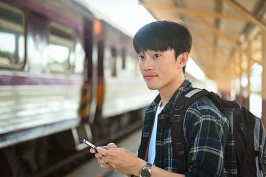 Attractive man using mobile phone during waiting for train at railway station.