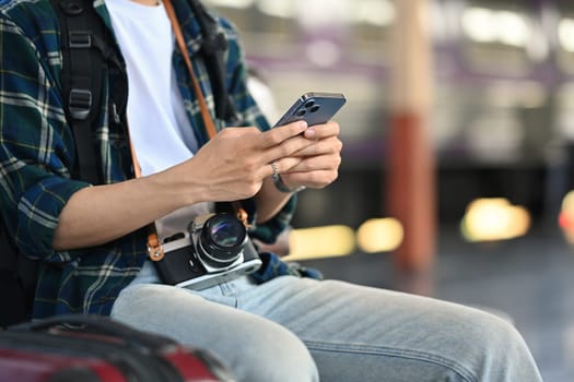 Cropped shot of male traveller using mobile phone during waiting for train at railway station.