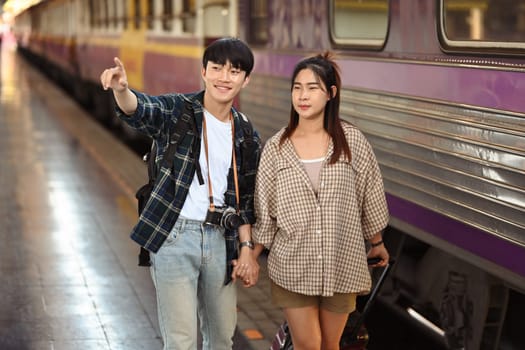 Happy young male and female tourist walking with a luggage walking at railroad station platform.